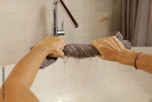 Photos A person wringing out a wet towel over a bathtub.