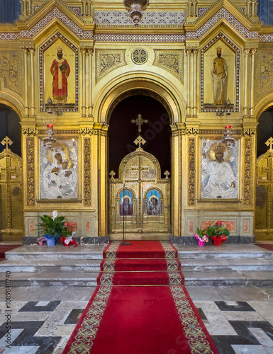 Trieste, Italy - June 27, 2024: Serbian Orthodox Church of Saint Spyridon. Center of the golden Iconostasis filled with paintings, icons on gold and silver. Red carpet leads to center doorway