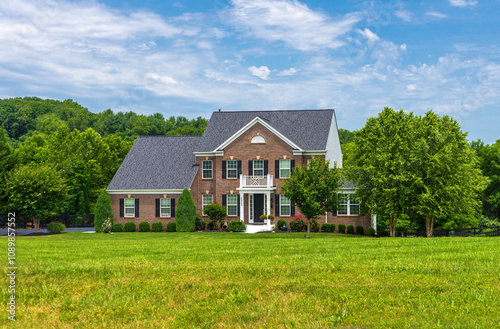 Beautiful brick country house with trees and a spacious green lawn in the foreground. photo