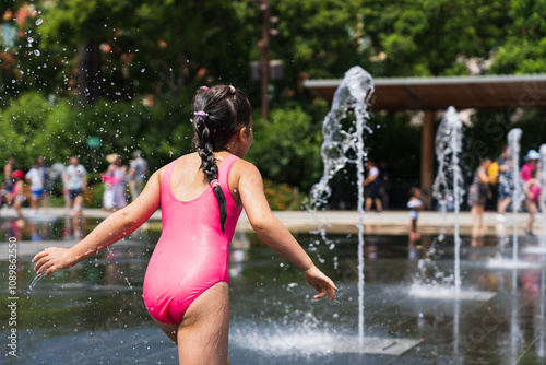 A child girl in a pink swimsuit plays with fountains in the city of Nice in southern France on a summer day. photo