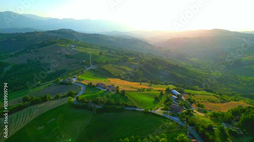 Gorgeous aerial push-in and pedestal down shot from Monte San Martino, scattered houses, buildings and winding roads sit amongst placid Marche hillscapes, thickets, Sibillini Mountains, in golden hour photo