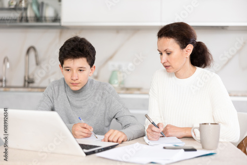 Boy and his mother study via video conference using a laptop in kitchen photo