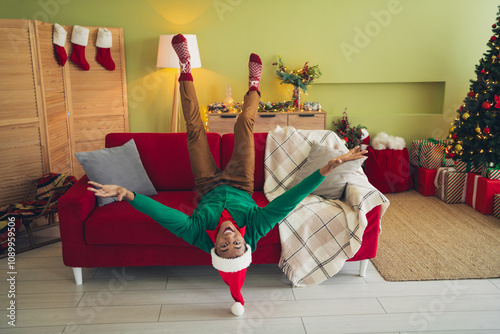 Full length photo of funky young mister lying sofa upside down wear green christmas garment tradition atmosphere decor house indoors room