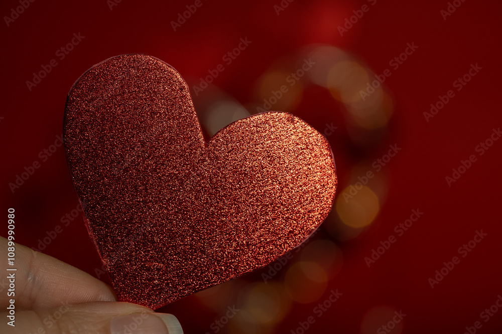 Obraz premium Dedos sosteniendo forma de corazón con textura granulada brillante roja