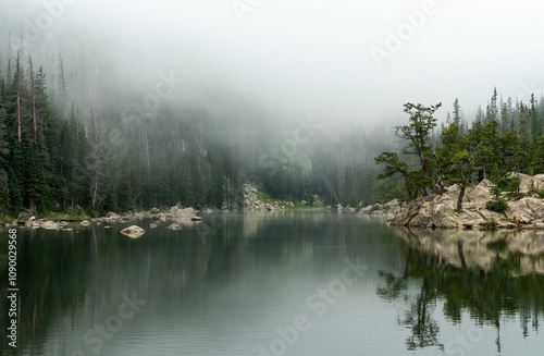 A misty morning at the tranquil lake surrounded by lush trees and rocky shores in a serene wilderness setting