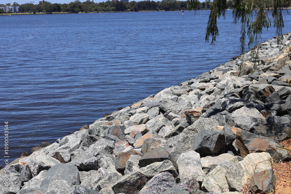large rock retaining wall reducing erosion beside blue water in bright sunshine