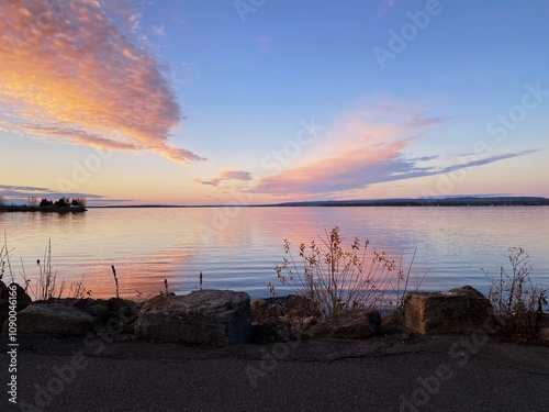 A breathtaking sunset over the Ottawa River, Canada, with soft pastel colors reflected in the calm water. The horizon and scattered clouds create a serene and tranquil atmosphere