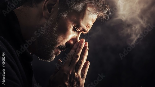 Close-up of a man praying with hands together, tears on his face, eyes closed, in a dark background with a heavenly light shining softly