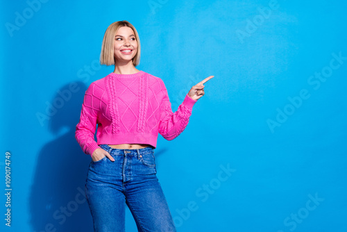 Photo of pretty young woman direct finger empty space ad wear pink pullover isolated on blue color background