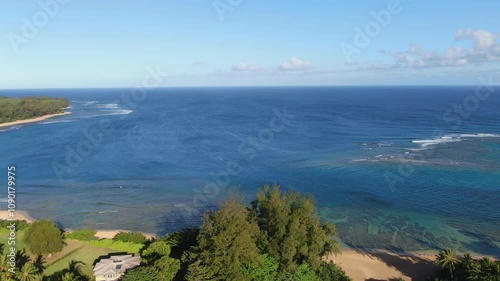 Aerial footage of Kauai's Tunnels Beach during sunrise, with sunny skies and clear, peaceful waters photo