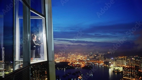 Mid adult businesswoman standing in a corporate windows with view of the city, talking on her mobile phone