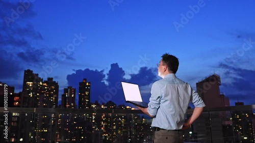 Young asian businessman with laptop on the building rooftop at city night