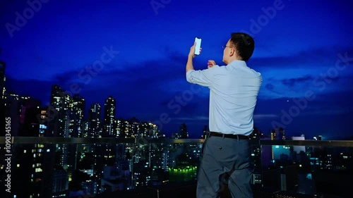 Young asian businessman using mobile phone on rooftop skyscraper at night