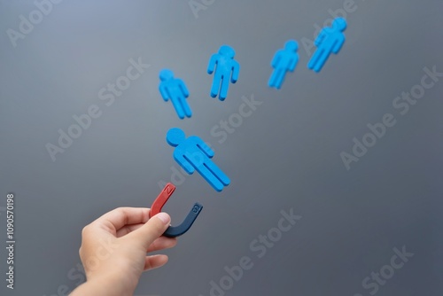 A hand holding a magnet attracts blue wooden figures. Attraction concept.
