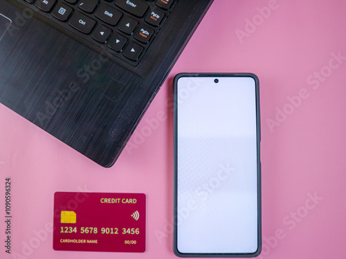 Credit cards, smartphone with blank screen and laptop on a pink background, representing technology and finance photo