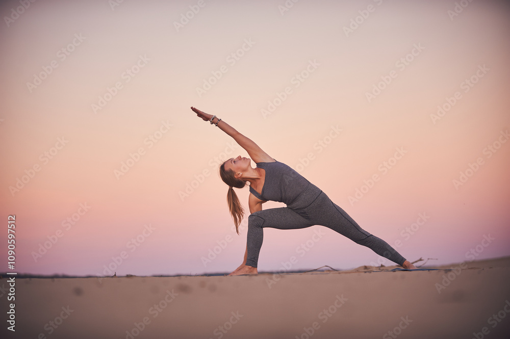 Fototapeta premium Yoga practitioner performs side angle pose during sunset on serene beach