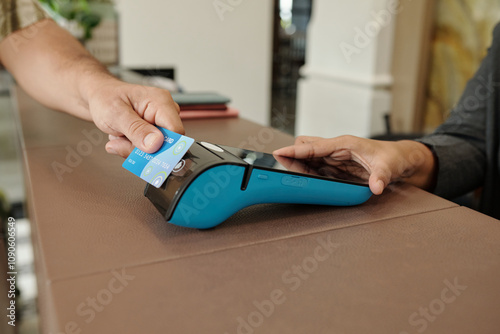 Hand holding credit card making payment on modern digital payment terminal with another hand receiving card transaction. Close-up of cashless transaction in progress at counter