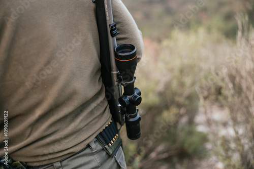 Hunter wearing rifle with scope walking through woods photo