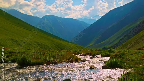 mountain river flowing down between green foothills at summer afternoon.