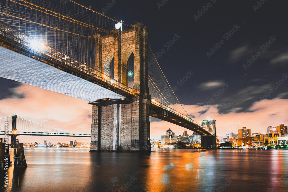 Fototapeta premium A long exposure of the Brooklyn bridge and Manhattan bridge with downtown Brooklyn in the background, over the East river with fast moving night clouds.