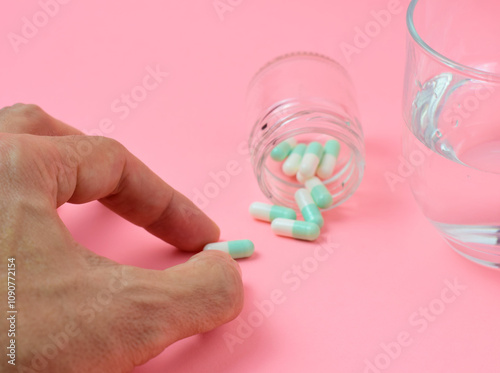 Hand of a person taking a pill, together with a container with more medication and a glass of water. Concept of medicine to cure.