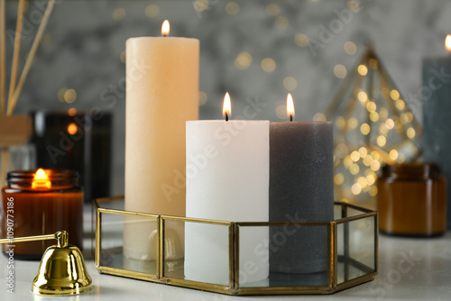 Beautiful burning candles on light table against blurred lights, closeup photo