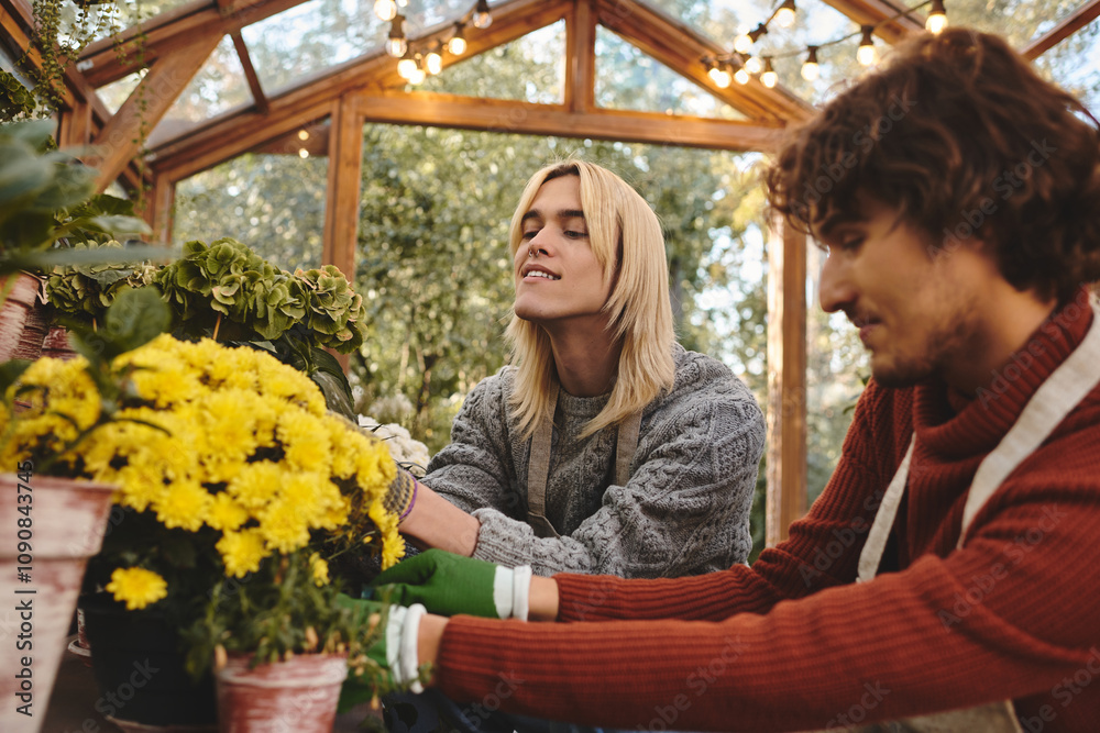Fototapeta premium In a lively greenhouse, a young lgbt couple shares a joyful moment while tending to vibrant yellow flowers. Their smiles reflect the happiness of nurturing plants in the warm sunlight.