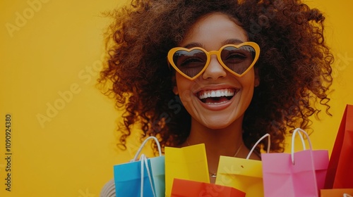 A woman with curly hair and heart-shaped sunglasses is smiling widely and holding several colorful shopping bags. She is standing against yellow background, suggesting a joyful shopping experience.