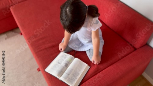 Zoom of a girl reading her Bible sitting on a couch in her living room