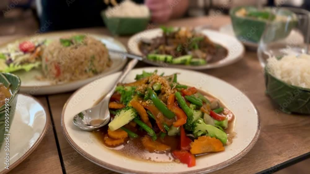Delicious spread of vibrant Thai cuisine on a wooden table, featuring stir-fried vegetables, fried rice, curry, and steamed rice in traditional banana leaf bowls.