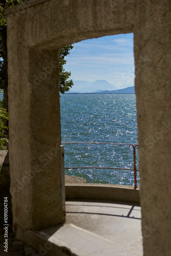 Picturesque View of Bodensee Through Medieval Castle Arch in Lindau, Germany. Stunning Summer Landscape Featuring Ancient Tower, Yacht, and Alpine Mountains.