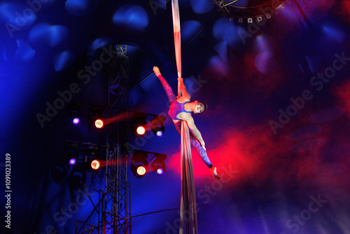 Aerialist performs a dangerous trick on a fabric high under dome of the circus under the spotlight. photo