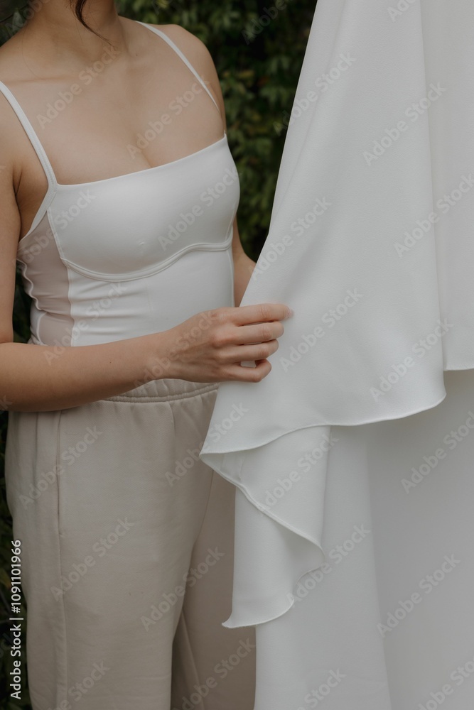Closeup vertical shot of a young woman standing and softly touching her hanging wedding dress Closeup vertical shot of a young woman standing and softly touching her hanging wedding dress