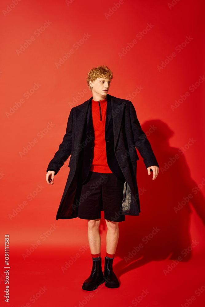 Standing against a vibrant red backdrop, a man showcases contemporary holiday fashion with a layered look. Standing against a vibrant red backdrop, a man showcases contemporary holiday fashion with a layered look.