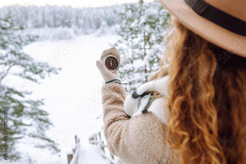 Woman holding a navigational compass on background of a snowy winter forest. Concept of direction, orientation, travel.