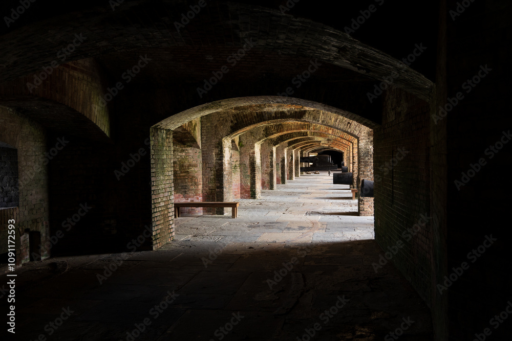 Fototapeta premium Historical brick fort with arched corridors, antique cannons, and weathered structures, showcasing intricate masonry and military architecture under natural light.