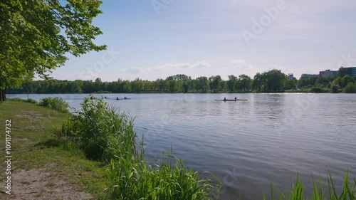 Kayaks on the pond in the city park. Residential buildings in the distance. Natural shore covered with grass
