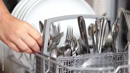 Female hand removing clean cutlery from a loaded dishwasher. Background of open wash machine 
