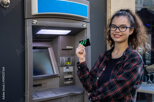 Young white girl withdraws money from an ATM while posing with her credit card