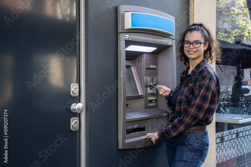 Young white girl withdraws money from an ATM while posing with her credit card photo