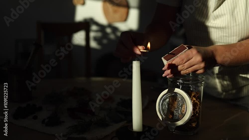 A woman lights a candle with a match, creating a cozy home atmosphere. Sunlight streams into the room, adding warmth and tranquility.