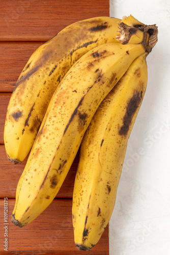 A small bunch of bananas on a wooden background and white background. Ripe fruit. Banana peel with spots. Healthy eating concept.