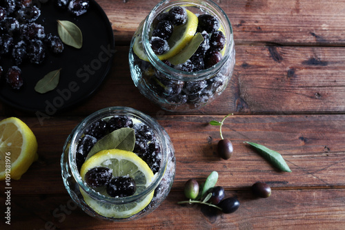 Olive nere fresche pronte per essere marinate in acqua, sale e limone in vasetti isolati su fondo di legno. photo