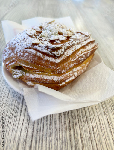 Deliziosa pasta sfoglia ripiena di crema e spolverata di zucchero in un piatto sul tavolo. Concetto di colazione italiana. photo