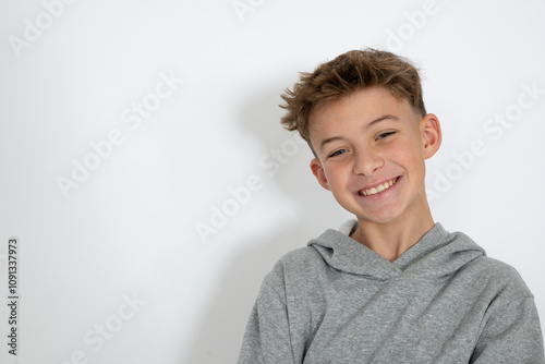 cool young 12 year old boy with grey hoody sweater posing in front of white background, having fun
