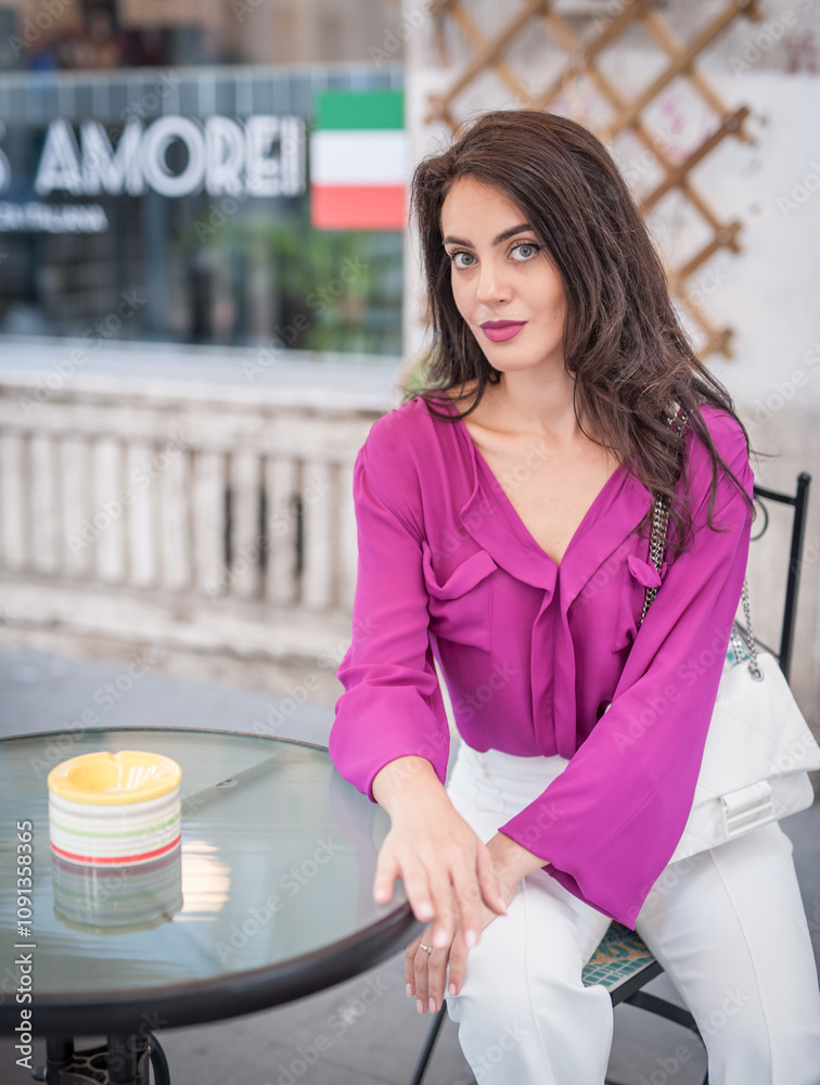 Beautiful young brunette woman in a purple blouse and white pants posing outdoor leans against a pillar .Portrait of a beautiful young brunette woman in a purple jacket posing