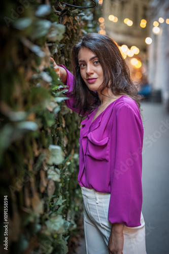 Obraz na płótnie Young beautiful brunette woman in a pink jacket and white pants posing on the street. Portrait of a beautiful young woman in a purple blouse and white pants posing in an outdoor cafe on the street w salonie