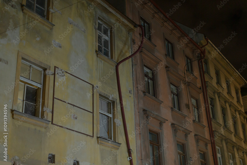 Fototapeta premium The breathtaking view of the night showcases two historic building facades that feature intricate details and visible utility pipes, all set against a lively and vibrant urban backdrop
