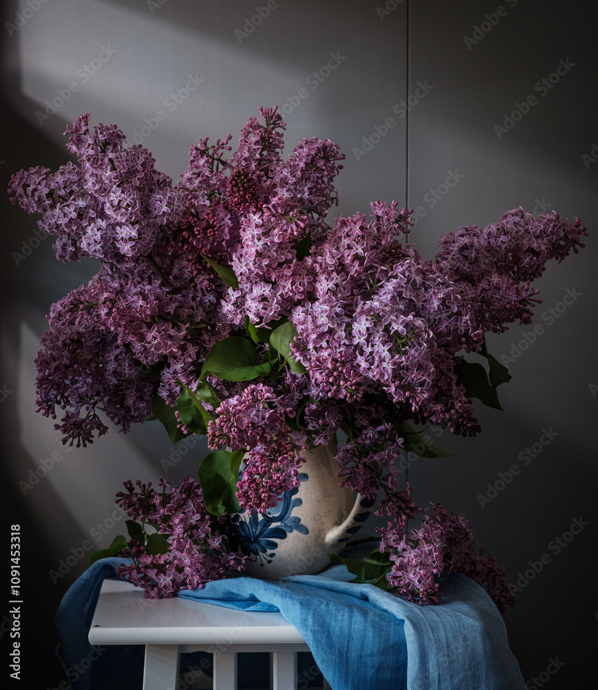 A beautiful arrangement of lilac flowers is displayed in a white vase on a table. The flowers are in full bloom and their vibrant color creates a sense of freshness and vitality.
