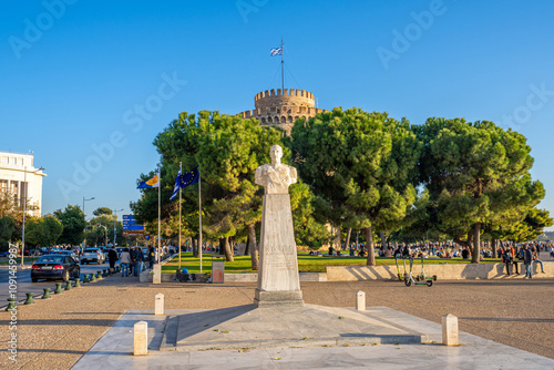 Bust of Nikolaos Votsis with the Iconic White Tower in the Background on a Bright Sunny Day in Thessaloniki, Greece, Surrounded by Lively City Scenes